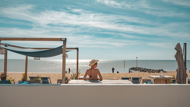 A beach view with a hammock, lounge chairs, and a table under a shaded area. - Hôtel Le Rivage (Chatelaillon-Plage)