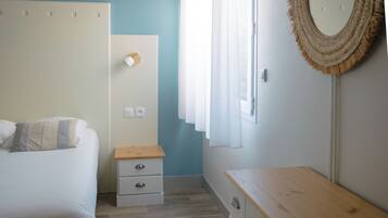 Une chambre à coucher comprenant un lit, une table de chevet, une commode, un miroir et une fenêtre avec des rideaux.