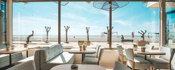 Restaurante à beira-mar com área externa, mesas e cadeiras, com vista para a praia e o oceano.