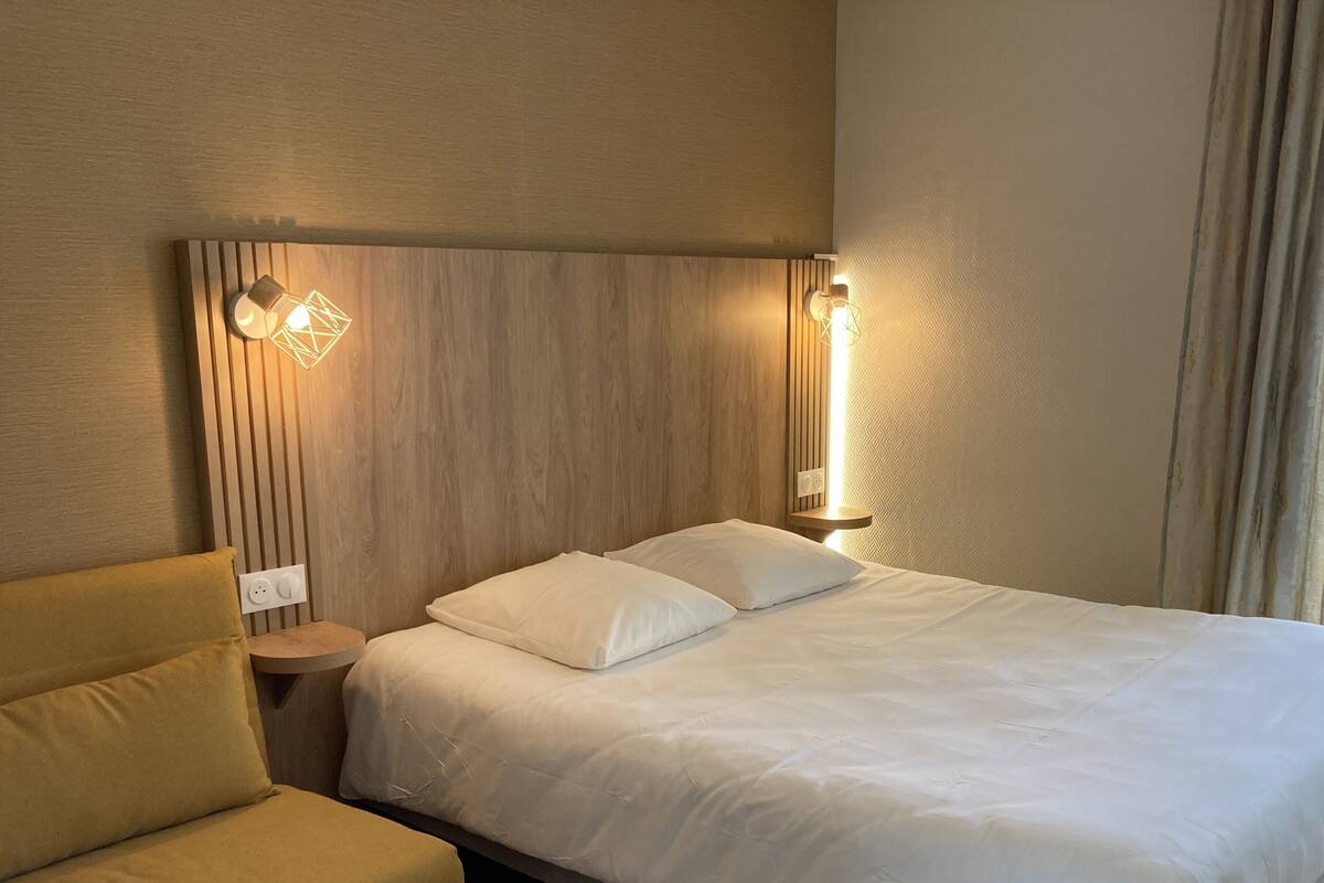 A hotel room with a bed, a nightstand, a lamp, and a chair.
