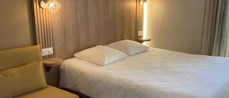 Una habitación de hotel con cama, mesita de noche, lámpara y una silla.
