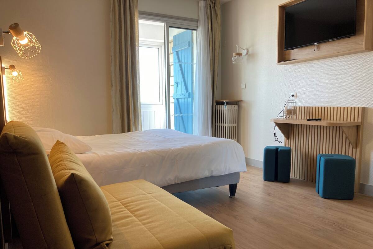 A hotel room with a bed, a sofa, a desk with a chair, and a TV mounted on the wall.