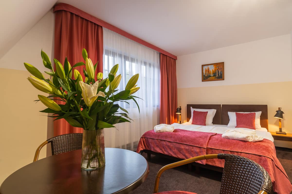 A hotel room with a bed, a dining table, and a vase of flowers.