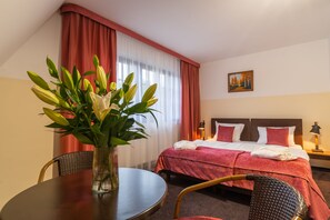 A hotel room with a bed, a dining table, and a vase of flowers.
