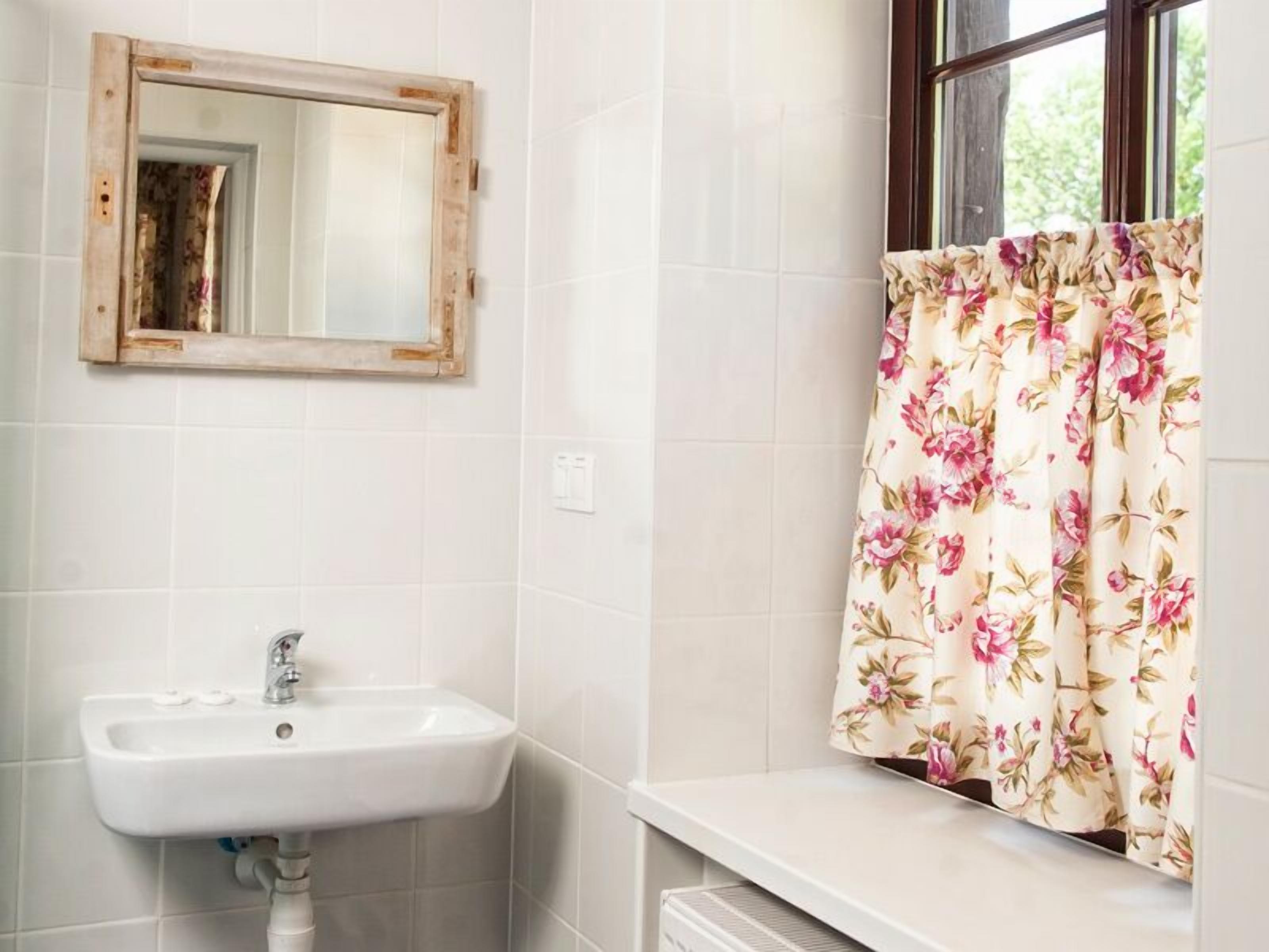 Un baño con un lavamanos blanco, un espejo y una ventana con cortinas florales.