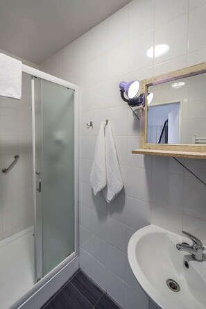 A bathroom with a glass shower enclosure, a white sink, and a mirror with lights.