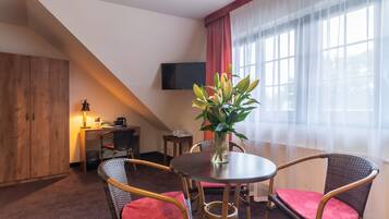 Une chambre d’hôtel équipée d’une table à manger, de chaises en osier, d’une plante en pot, d’un téléviseur et d’un bureau avec une lampe.