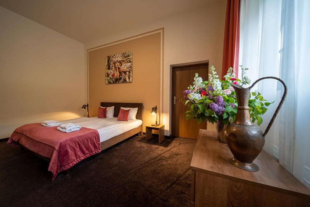 A hotel room with a bed, a nightstand, a lamp, a vase with flowers, and a painting on the wall.