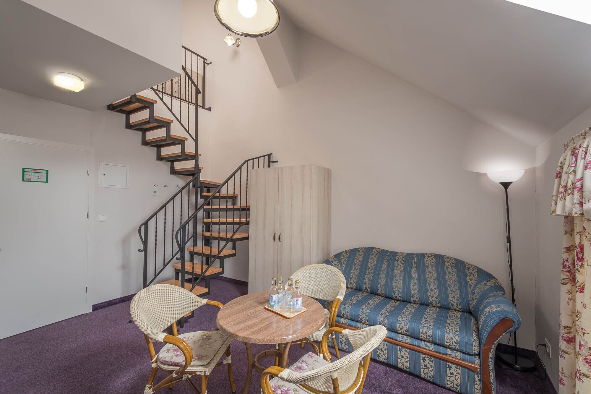 A living room with a wooden staircase, a sofa, and a round table with chairs.