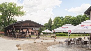 An outdoor seating area with tables and chairs, a wooden pavilion, and umbrellas with logos. - Folwark Książęcy (Osiecznica)