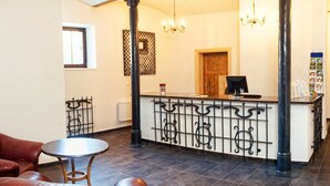 A reception area with a check-in counter, a leather sofa, a small round table, and a chandelier. - Folwark Książęcy (Osiecznica)