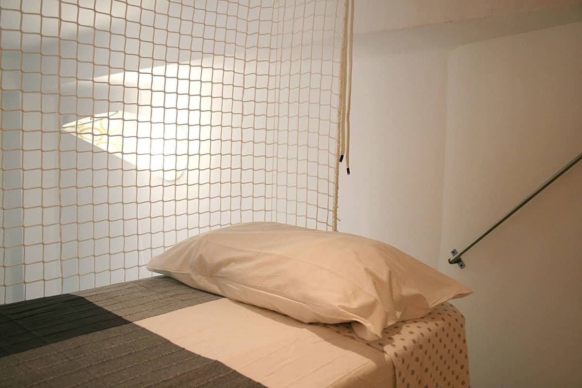 A bed with a beige mattress and a single pillow, a netted window, and a metal rod.