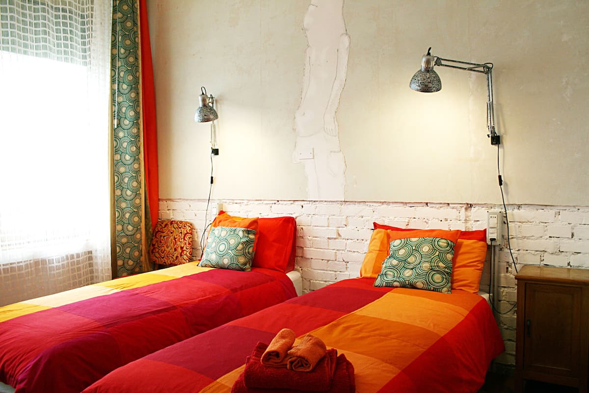 A room with two beds, each with a red and orange bedspread, and a wooden nightstand.