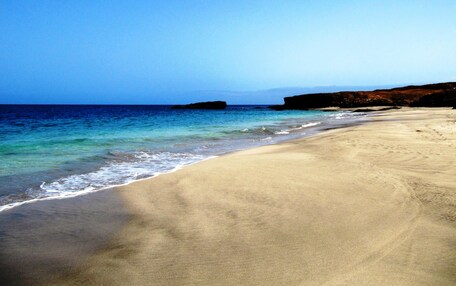 A beach with clear blue water, sandy shore, and rocky cliffs in the background.