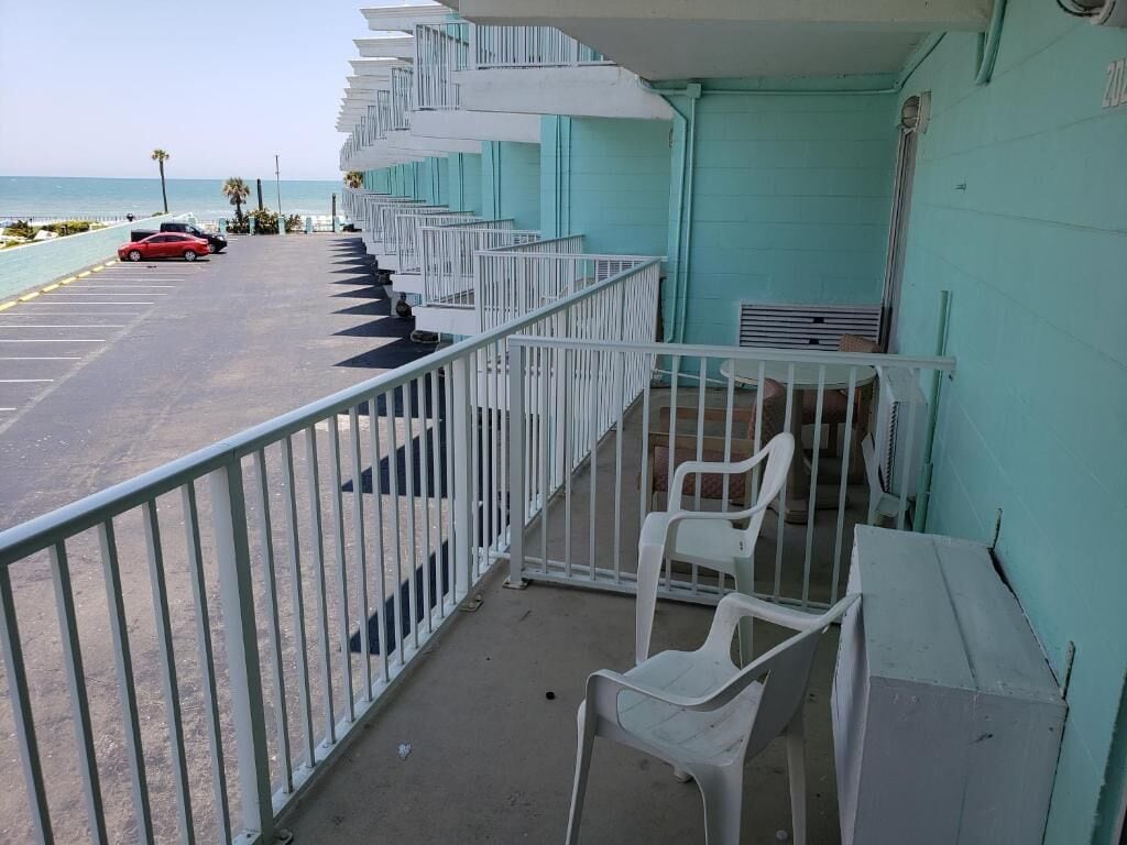 Ein Balkon mit weißen Geländern, der auf einen Parkplatz und einen Strand blickt.