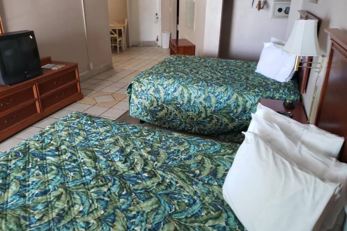 Hotellihuone, jossa on kaksi sänkyä, televisio, työpöytä ja lamppu.