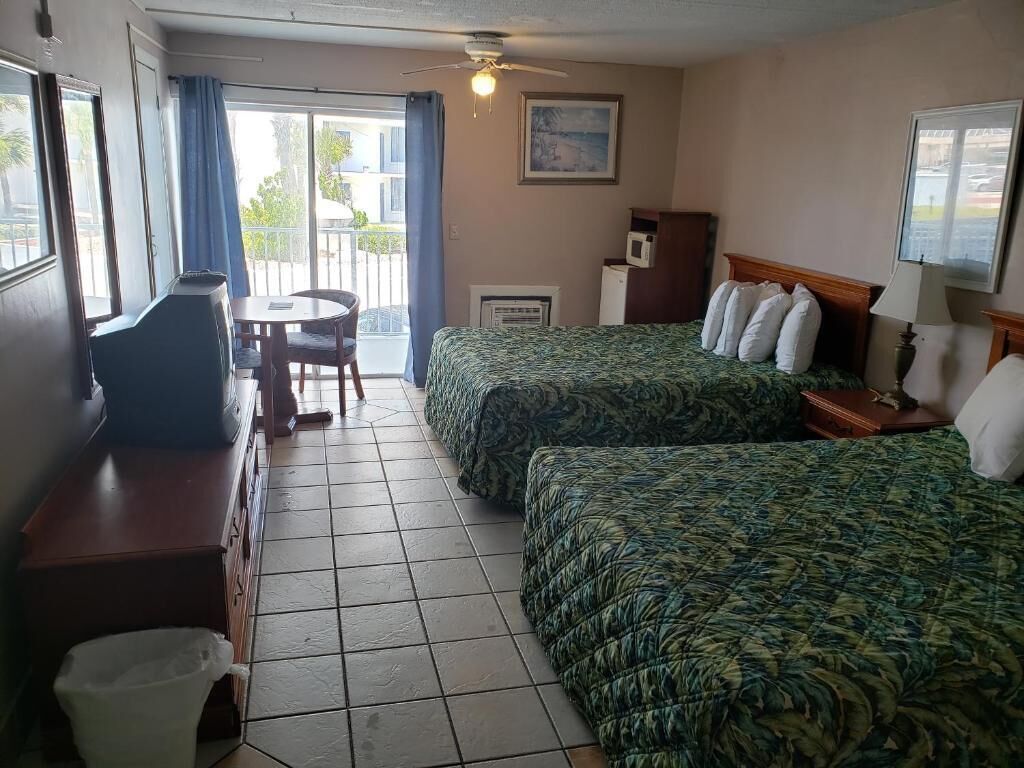 A hotel room with two beds, a desk, a chair, a ceiling fan, and a view of the outdoors.