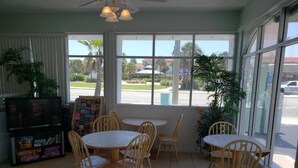 A room with a large window, a television, and several wooden tables and chairs. - The Seascape Inn (Daytona Beach Shores)