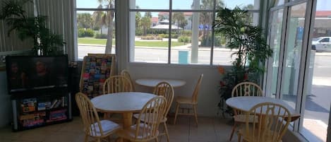 A room with a large window, a television, and several wooden tables and chairs.