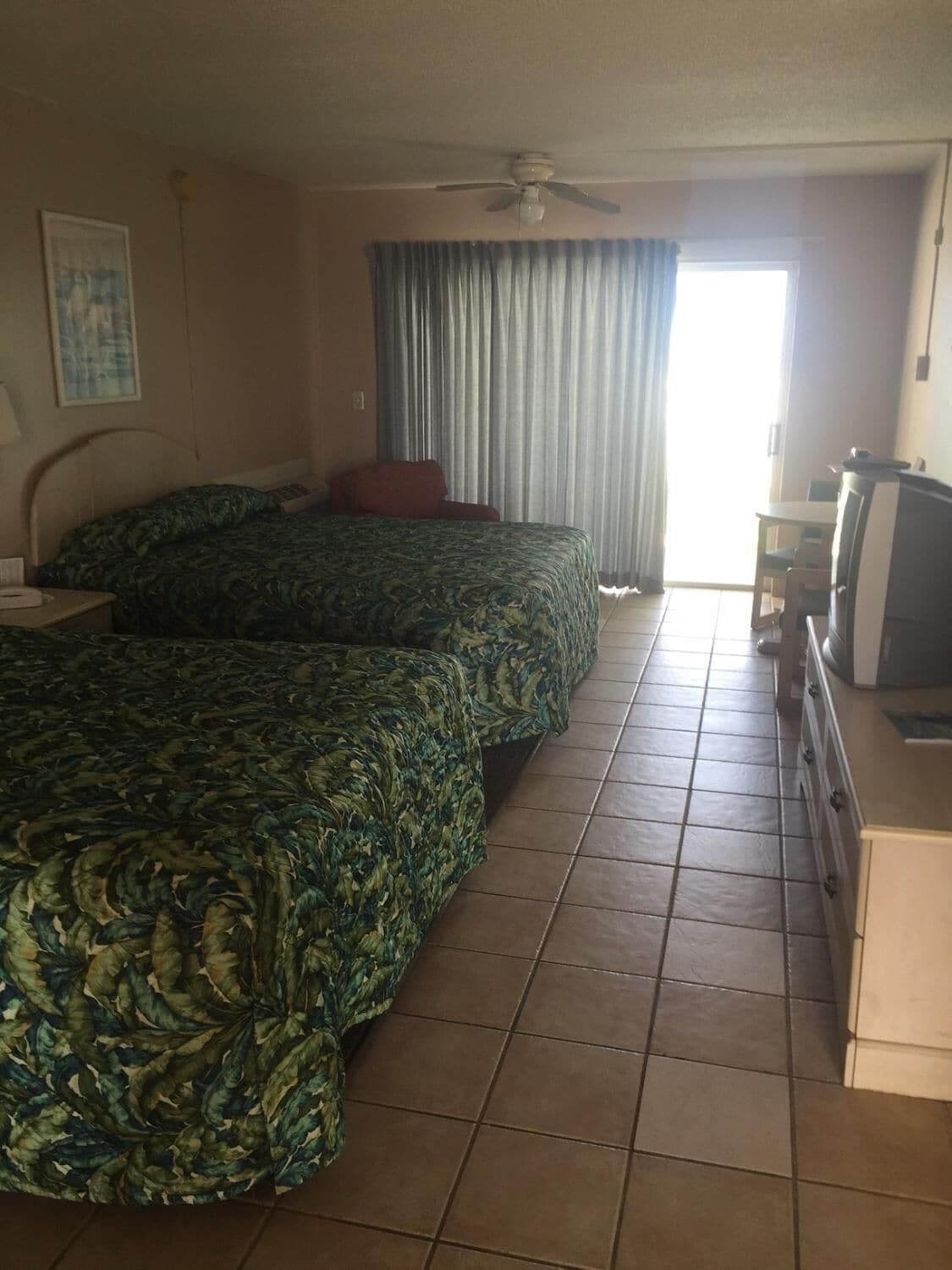 Een hotelkamer met twee bedden, een televisie, een bureau en een raam met gordijnen.
