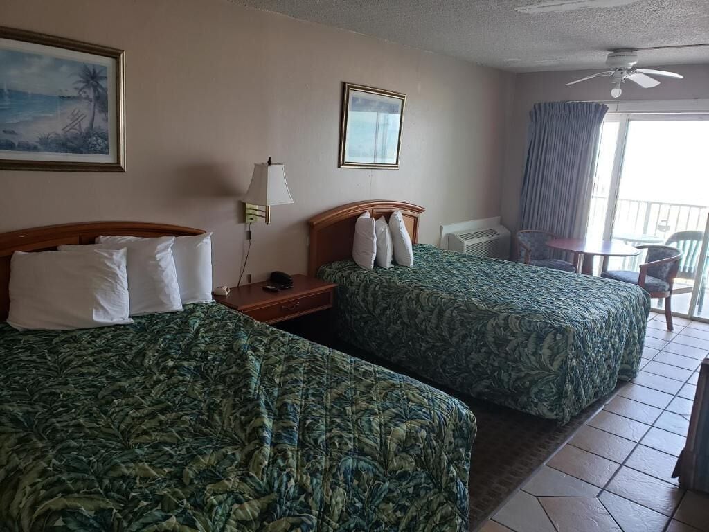 Habitación de hotel con dos camas, un balcón, ventilador de techo y vista al océano.
