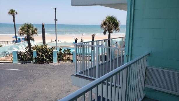 A balcony with a view of a beach, palm trees, and a pool area. - The Seascape Inn (Daytona Beach Shores)
