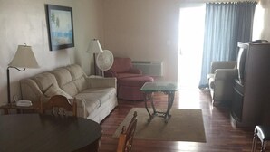 A living room with a wooden floor, a dining table with chairs, a sofa, a TV, and a fan. - The Seascape Inn (Daytona Beach Shores)