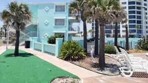 A hotel with a light blue exterior, palm trees, and a pool area with lounge chairs. - The Seascape Inn (Daytona Beach Shores)