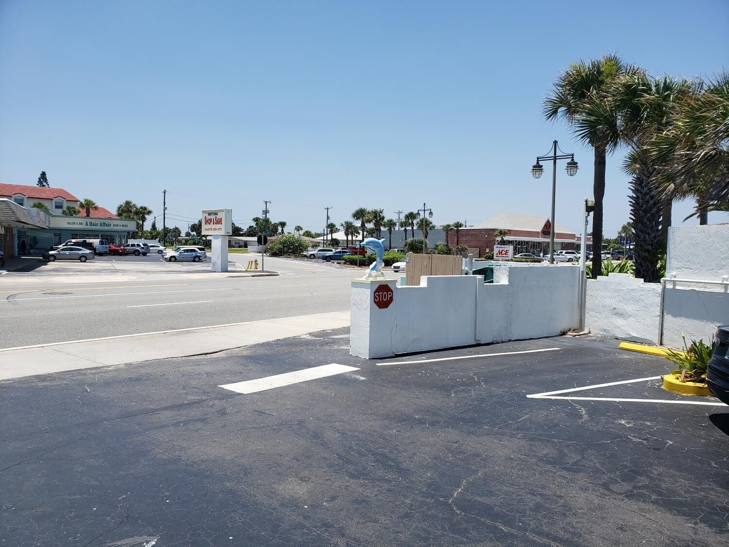 A parking lot with a stop sign, a white wall, and a palm tree.