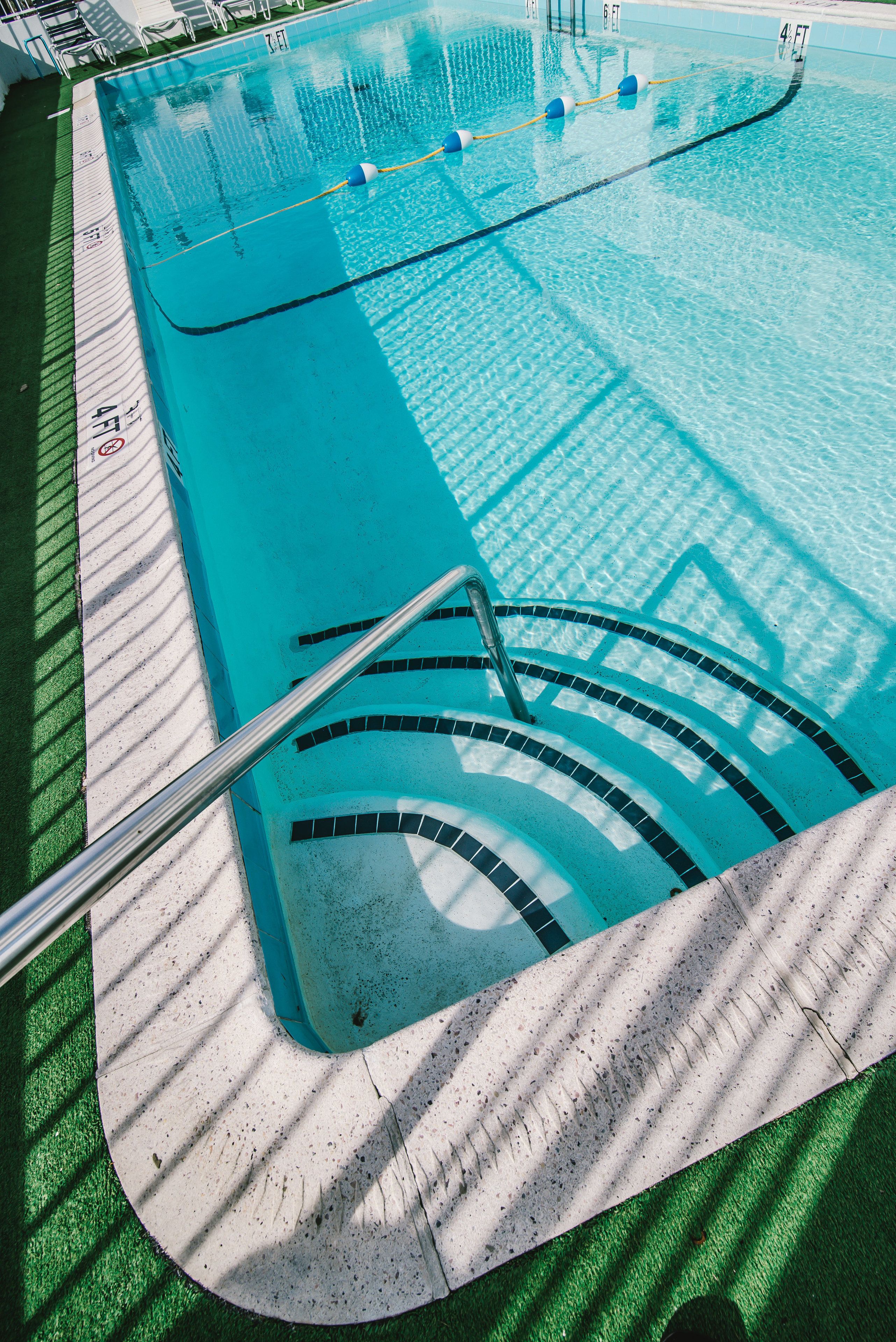 A swimming pool with clear blue water, a diving board, and a tiled deck area.