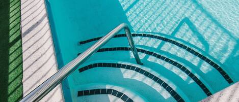 En swimmingpool med kristallklart blått vatten, en hoppställning och ett kaklat poolområde.