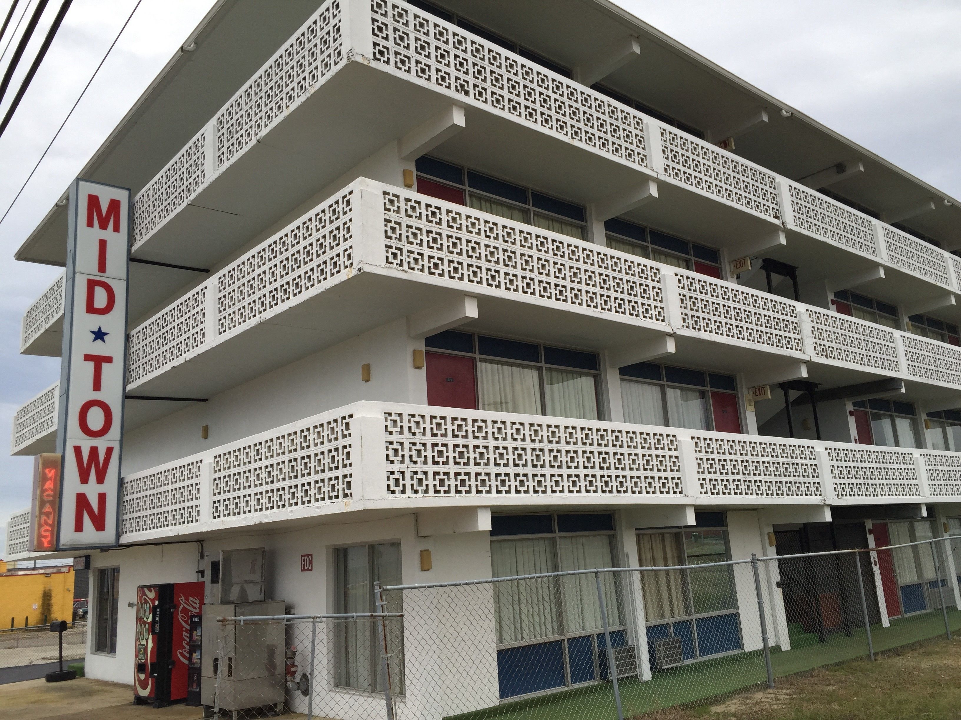 Een meerlaags gebouw met een opvallende geometrische gevel, een Coca-Cola automaat en een bord waarop 'MIDTOWN' staat.