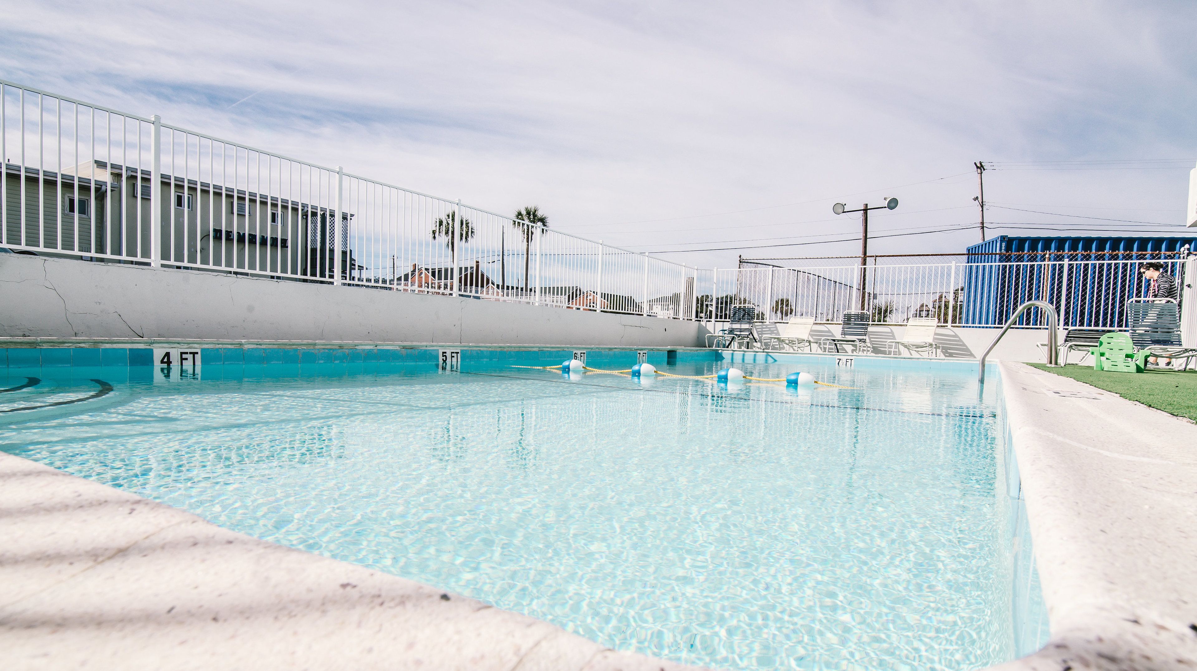 A swimming pool with lane markers, a white fence, and lounge chairs.