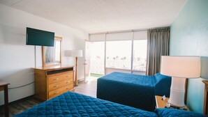 A hotel room with two beds, a dresser, a TV, and a balcony with curtains.