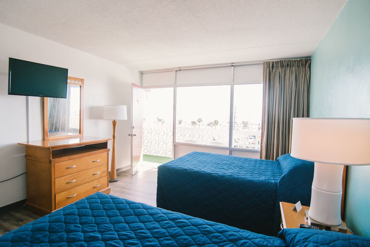 A hotel room with two beds, a dresser, a TV, and a balcony with curtains.