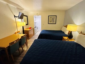 A hotel room with two beds, a desk, a chair, a TV, a lamp, and a framed picture on the wall.