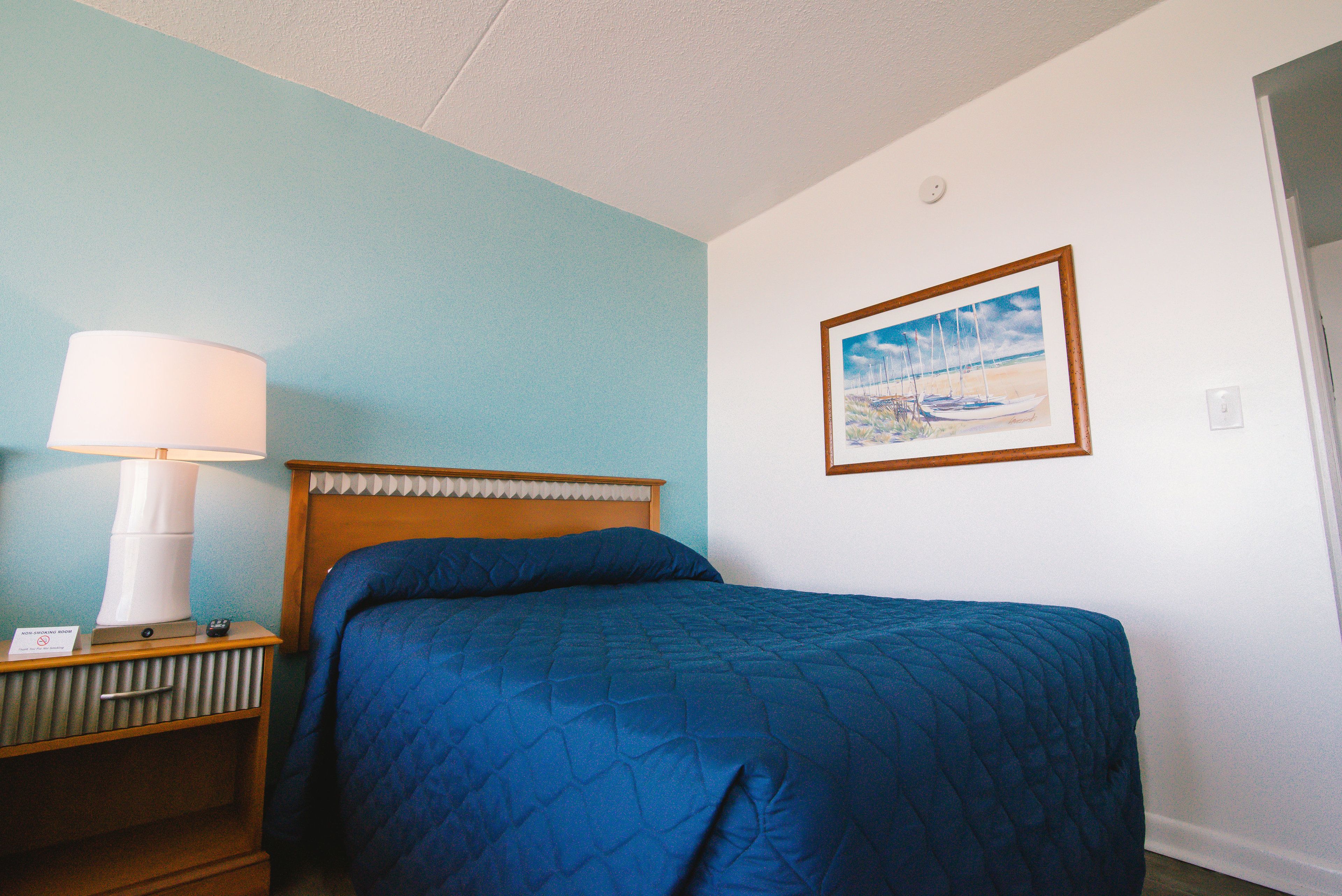 A hotel room with a bed, a nightstand with a lamp, and a framed picture on the wall.
