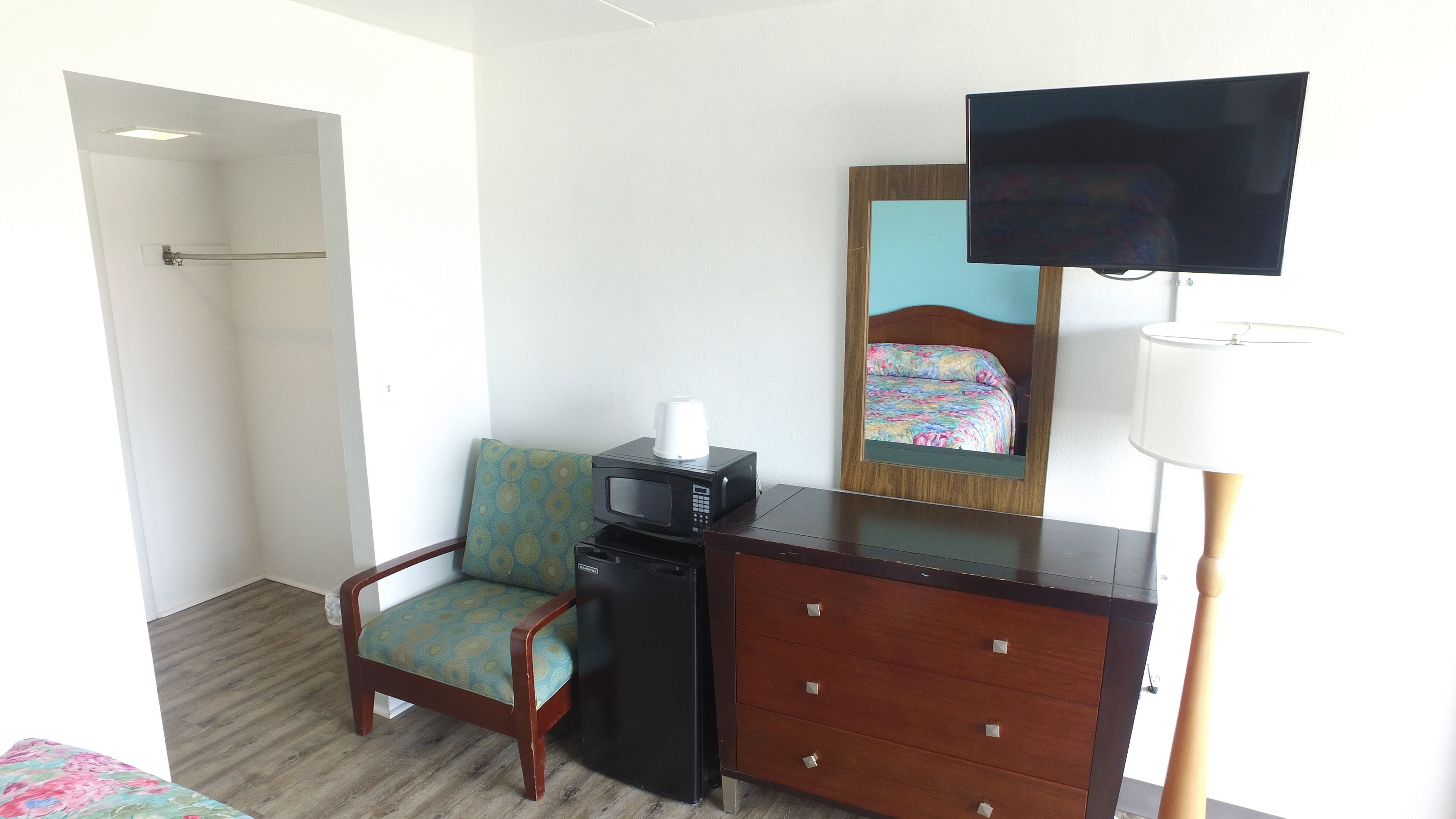 A hotel room with a wooden desk, a chair, a television, a microwave, and a bed with a floral bedspread.