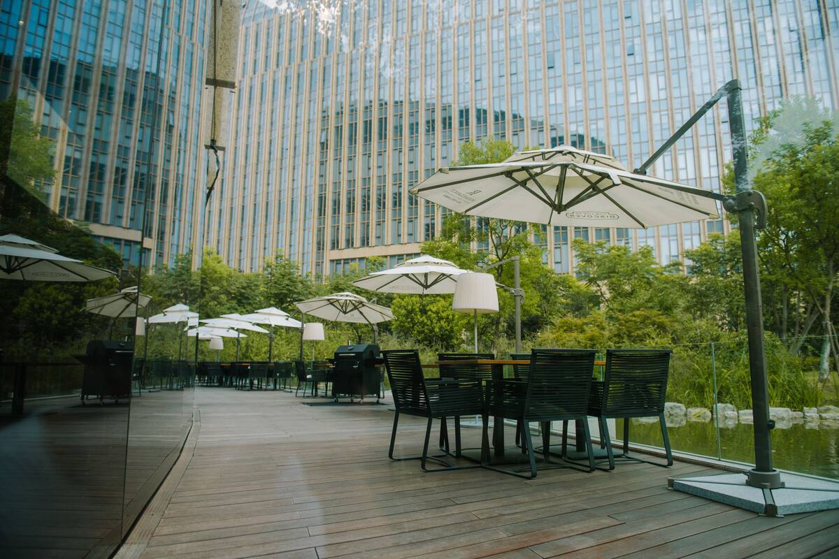 An outdoor patio area with wooden flooring, tables, chairs, and umbrellas.