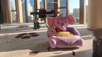 A plush toy elephant on a carpet with a floral pattern, a chair, and a table in a room with large windows.