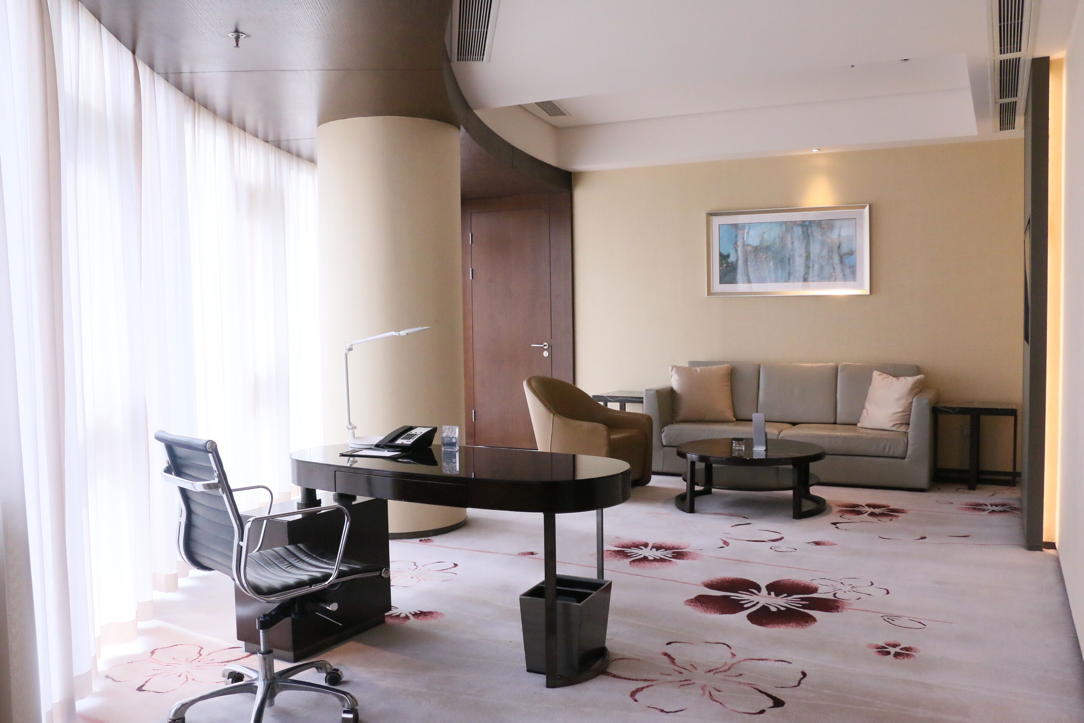 A hotel room with a desk, two chairs, a sofa, and a painting on the wall.