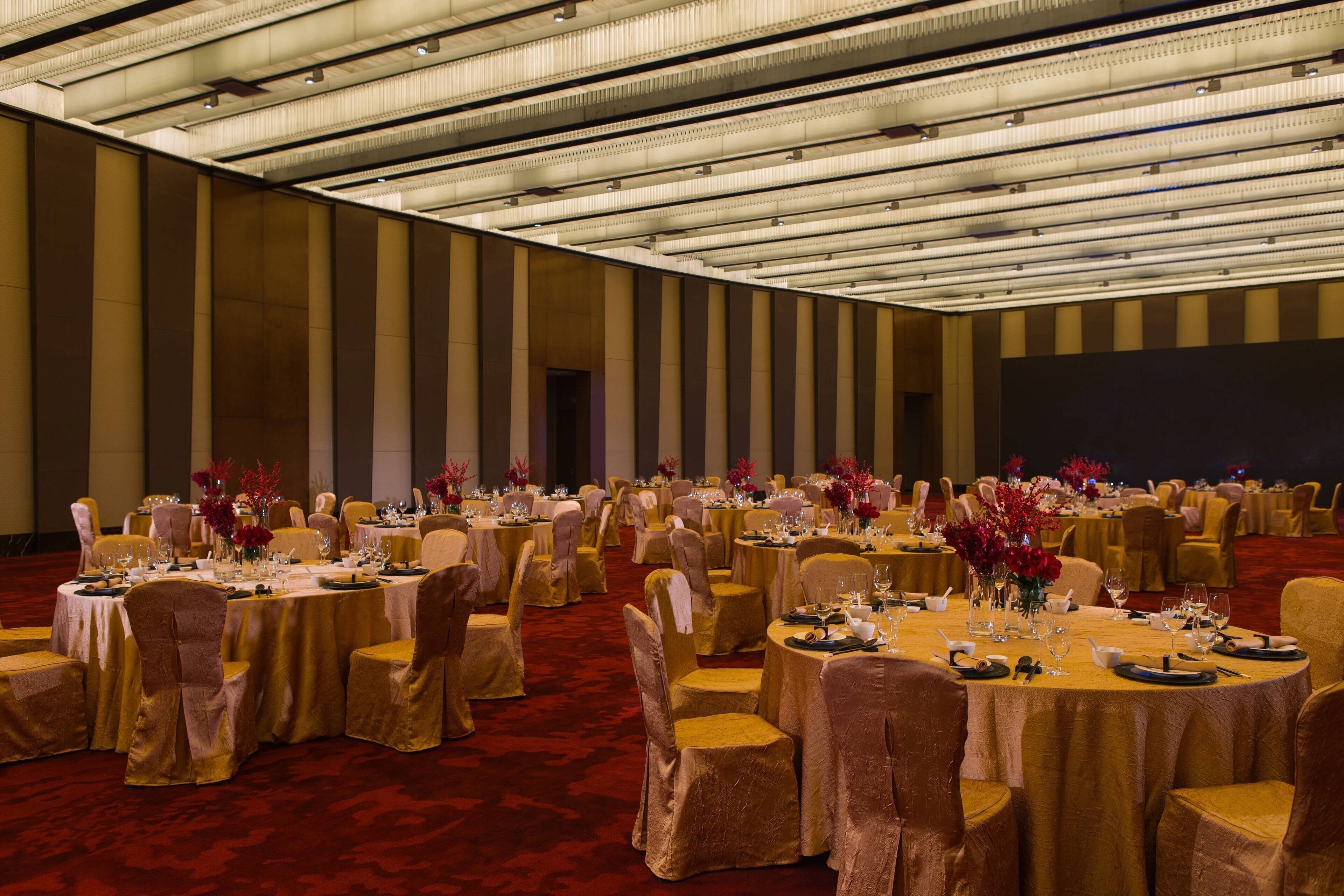 A banquet hall with round tables, chairs, and floral centerpieces.