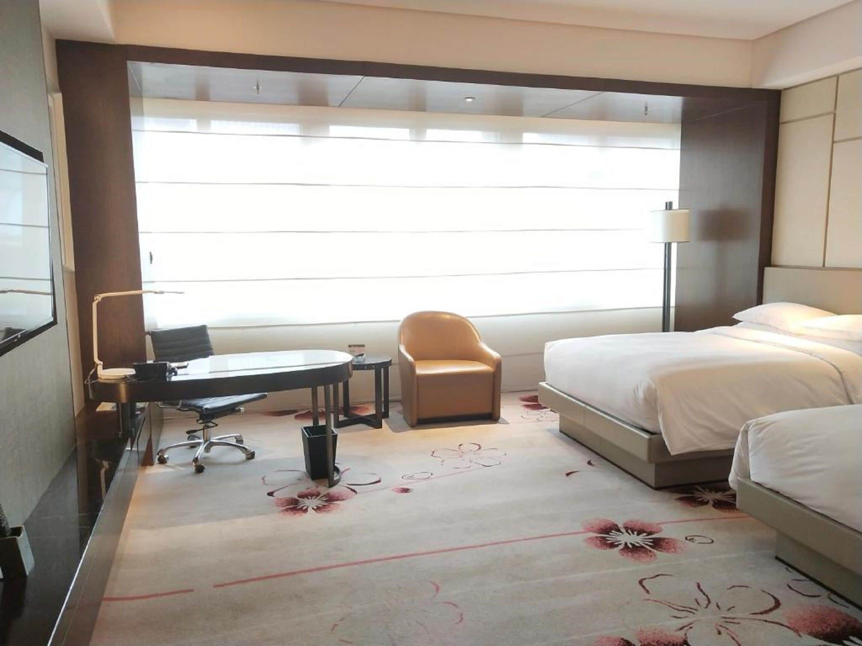 A hotel room with a bed, a desk, a chair, and a lamp.