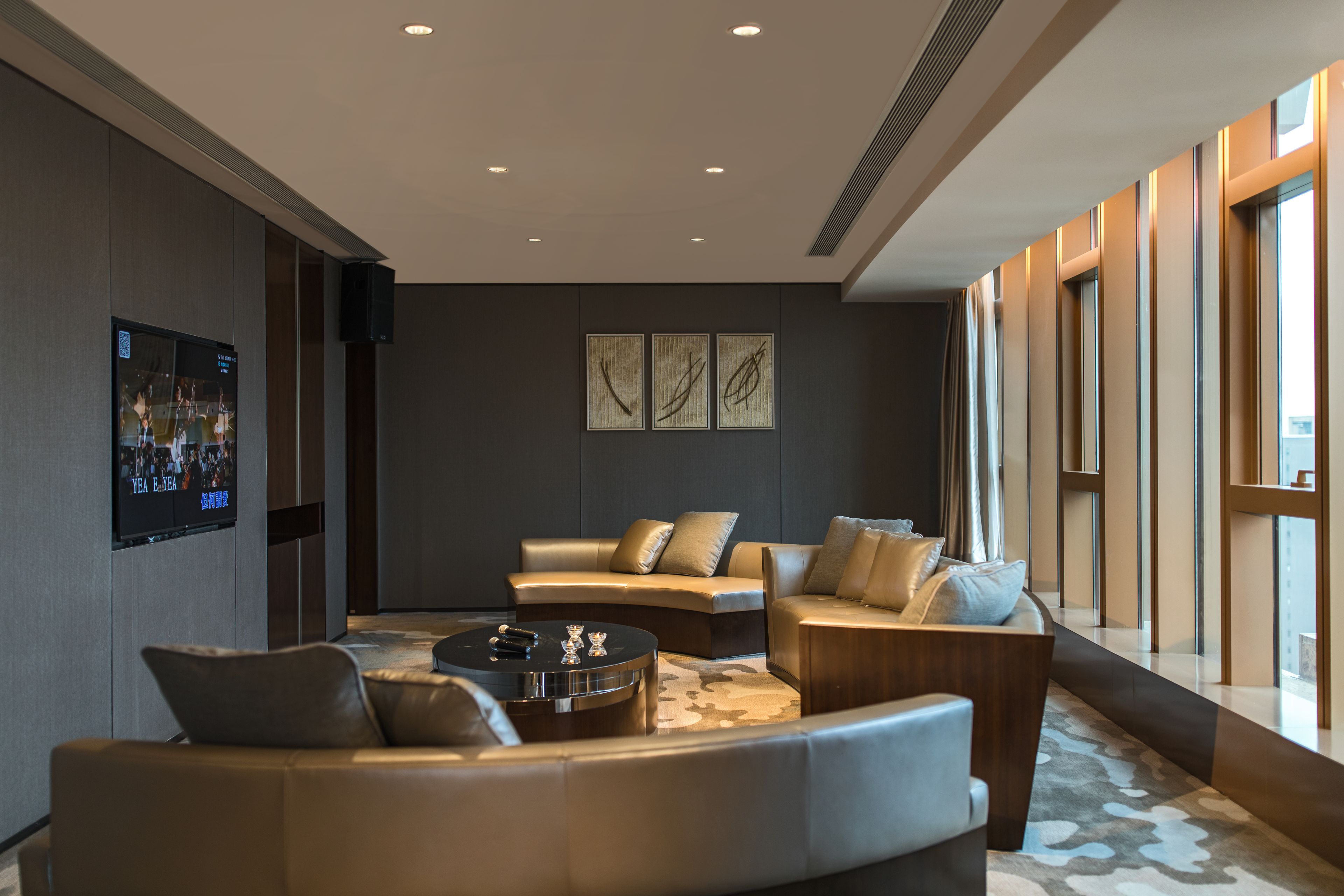 A modern living room with a curved sofa, a round coffee table, and a flat-screen TV mounted on the wall.