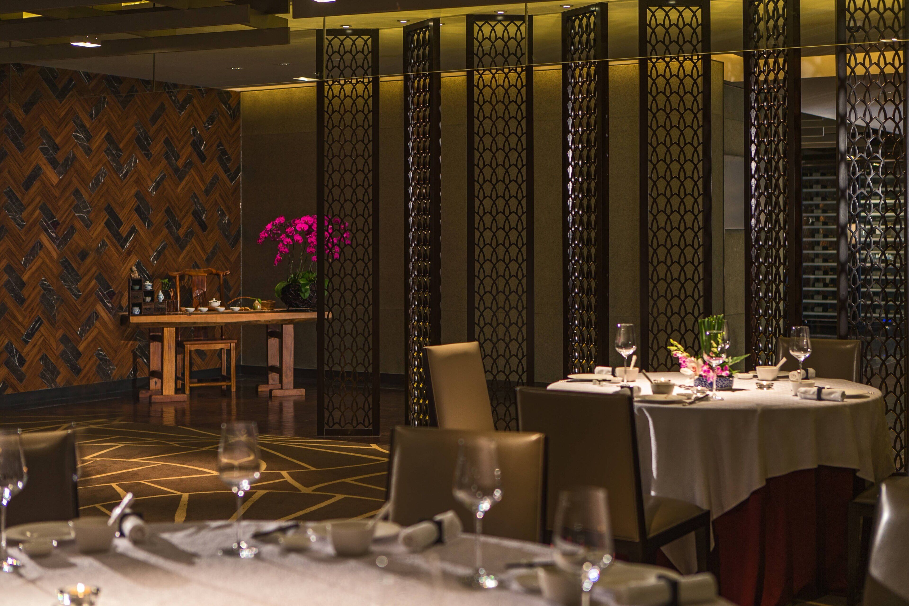 A restaurant with a herringbone patterned wall, a decorative partition with a lattice design, and a table set with wine glasses and a vase of flowers.