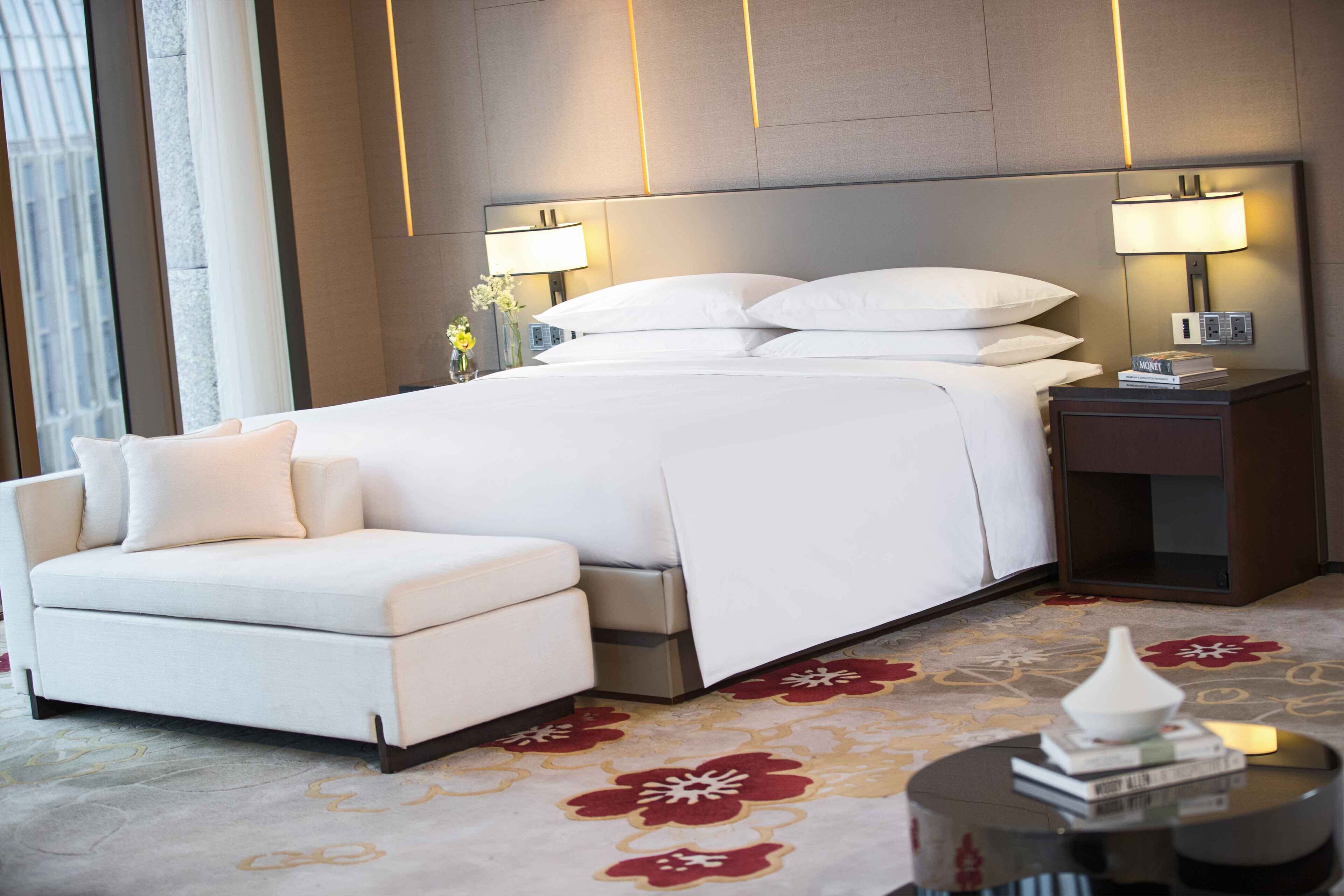 Een moderne hotelkamer met een groot bed, een slaapbank, twee nachtkastjes met lampen en een decoratieve vaas.