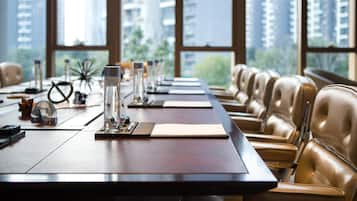 A conference room with a long table, leather chairs, and a view of tall buildings through large windows.
