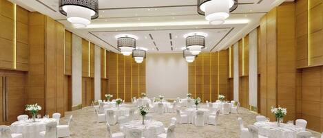 A spacious banquet hall with round tables, white chairs, and chandeliers.