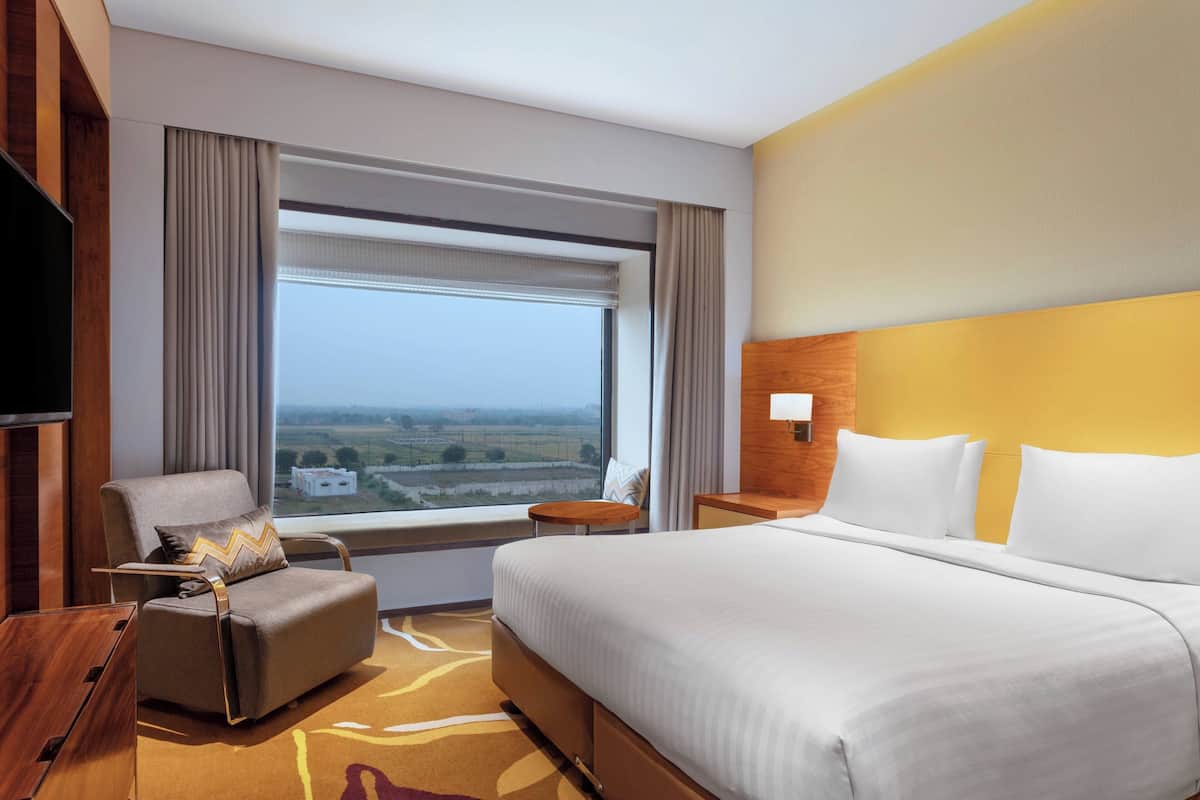 A hotel room with a large bed, a seating area with a chair, a small table, and a television.