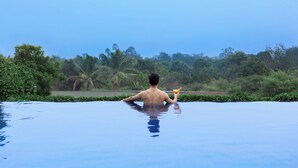 A man relaxing in a swimming pool with a drink, surrounded by lush greenery and a clear sky. - Courtyard by Marriott Raipur (Raipur)